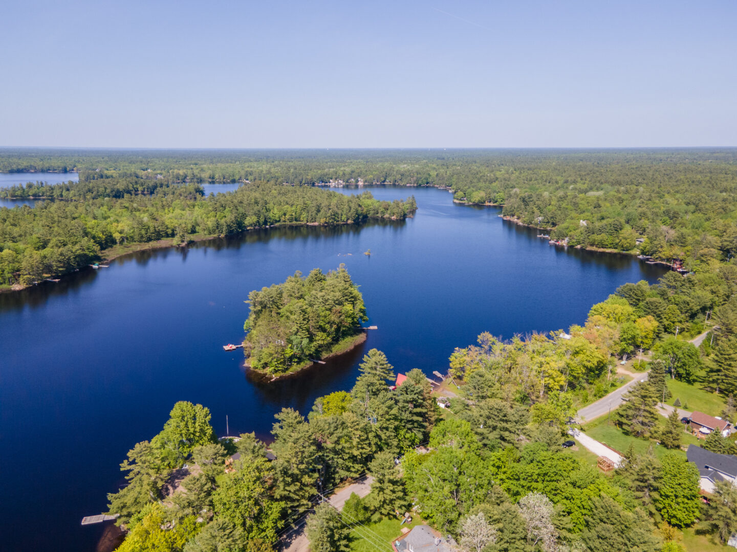 A wide stretch of deep blue lake with green trees on the land on either side. A small island with green trees sits in the middle.