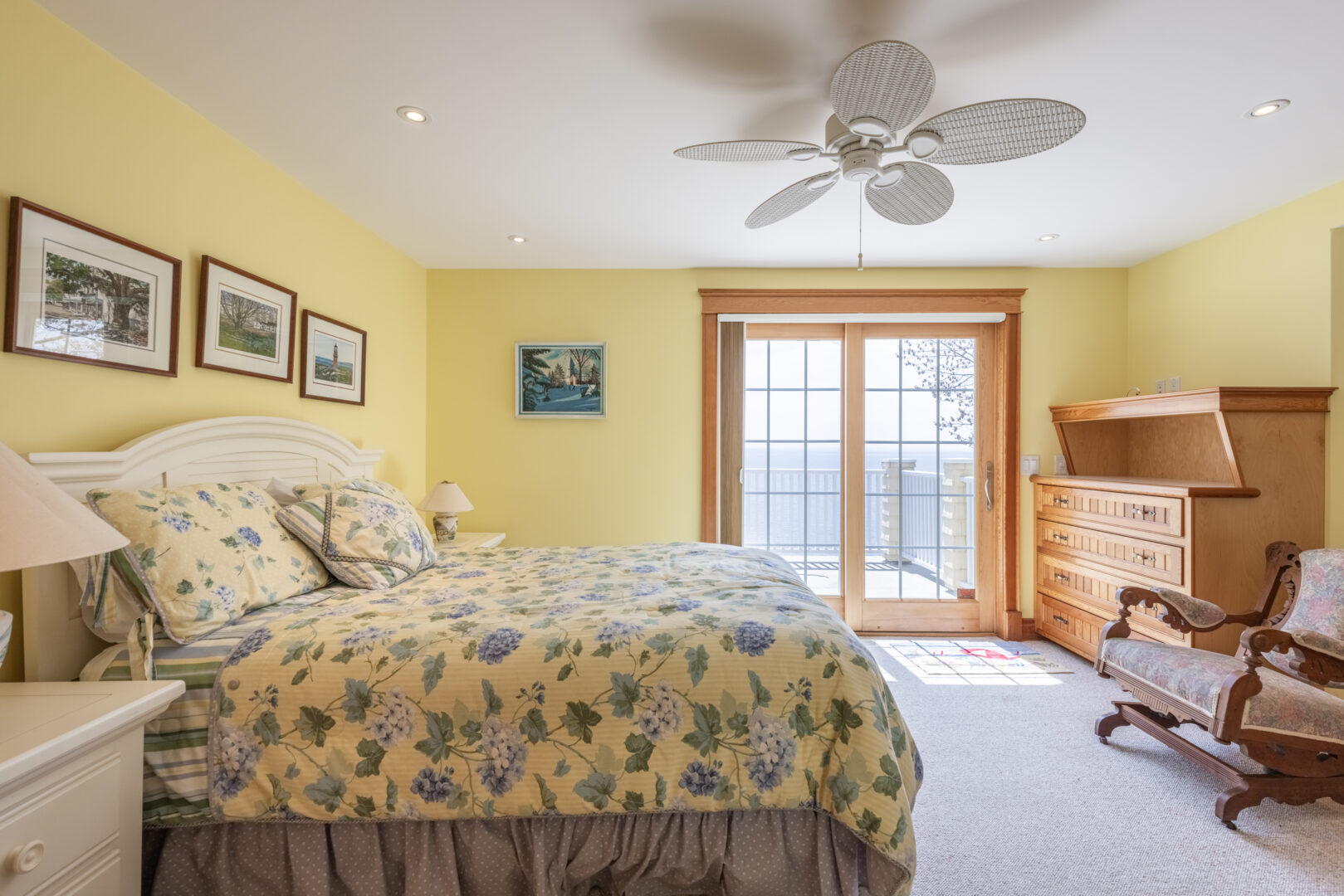 A large, bright bedroom with yellow walls, a big bed with a yellow floral bedspread, and double doors leading out to a balcony.