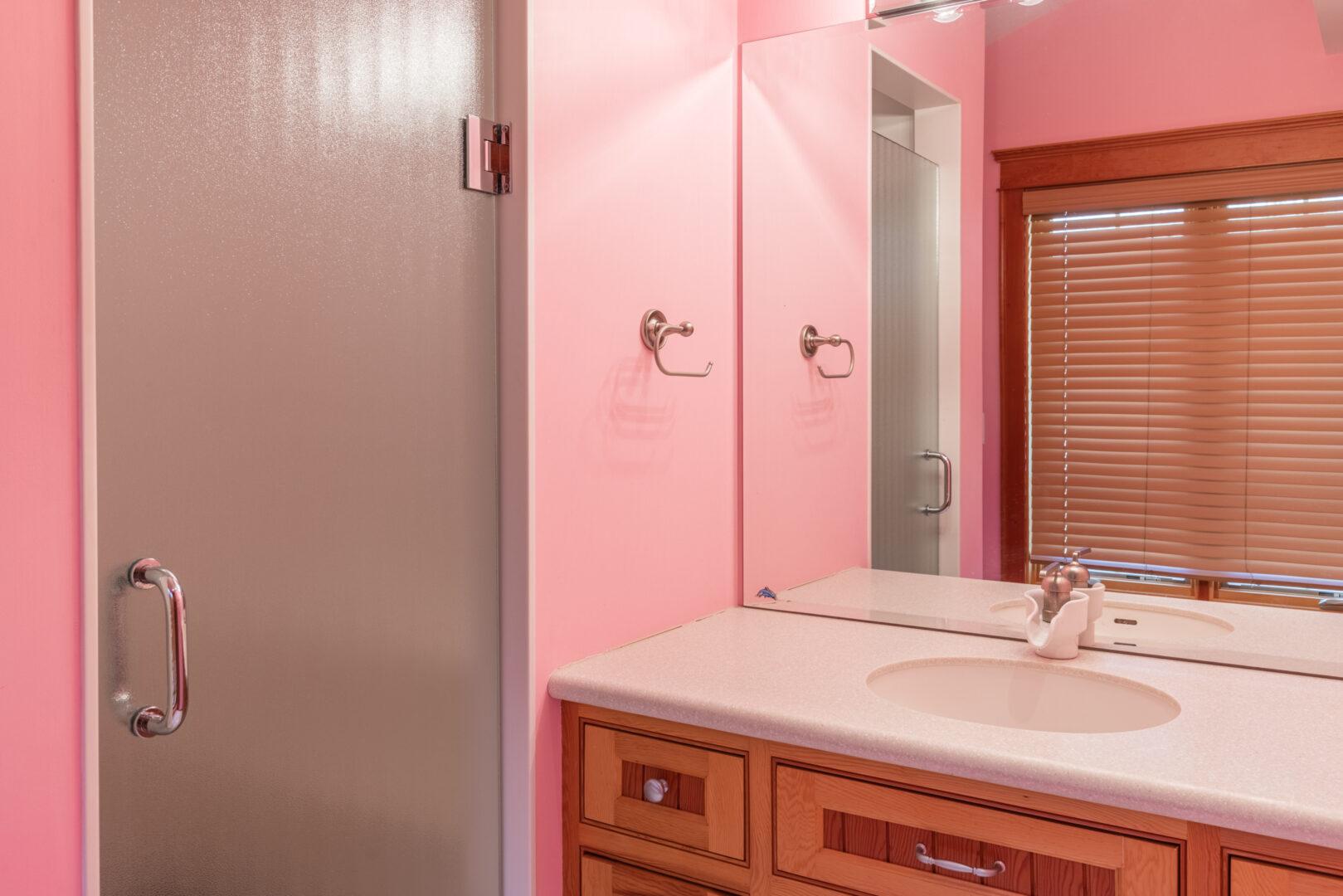A small bathroom with pink walls, a sink, and a walk-in shower.