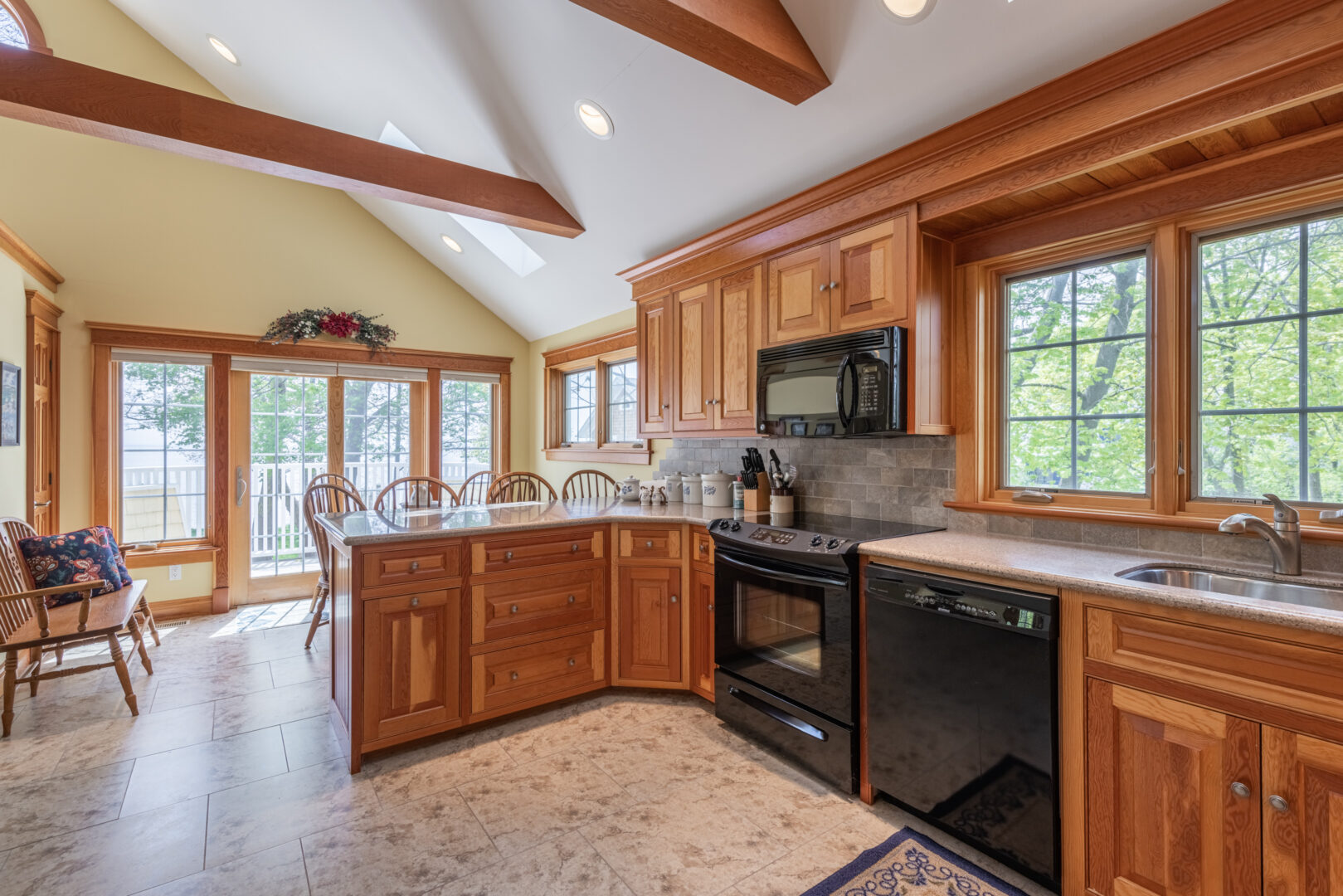 A bright kitchen area with warm wooden cabinets, black appliances, high ceilings and lots of natural light.