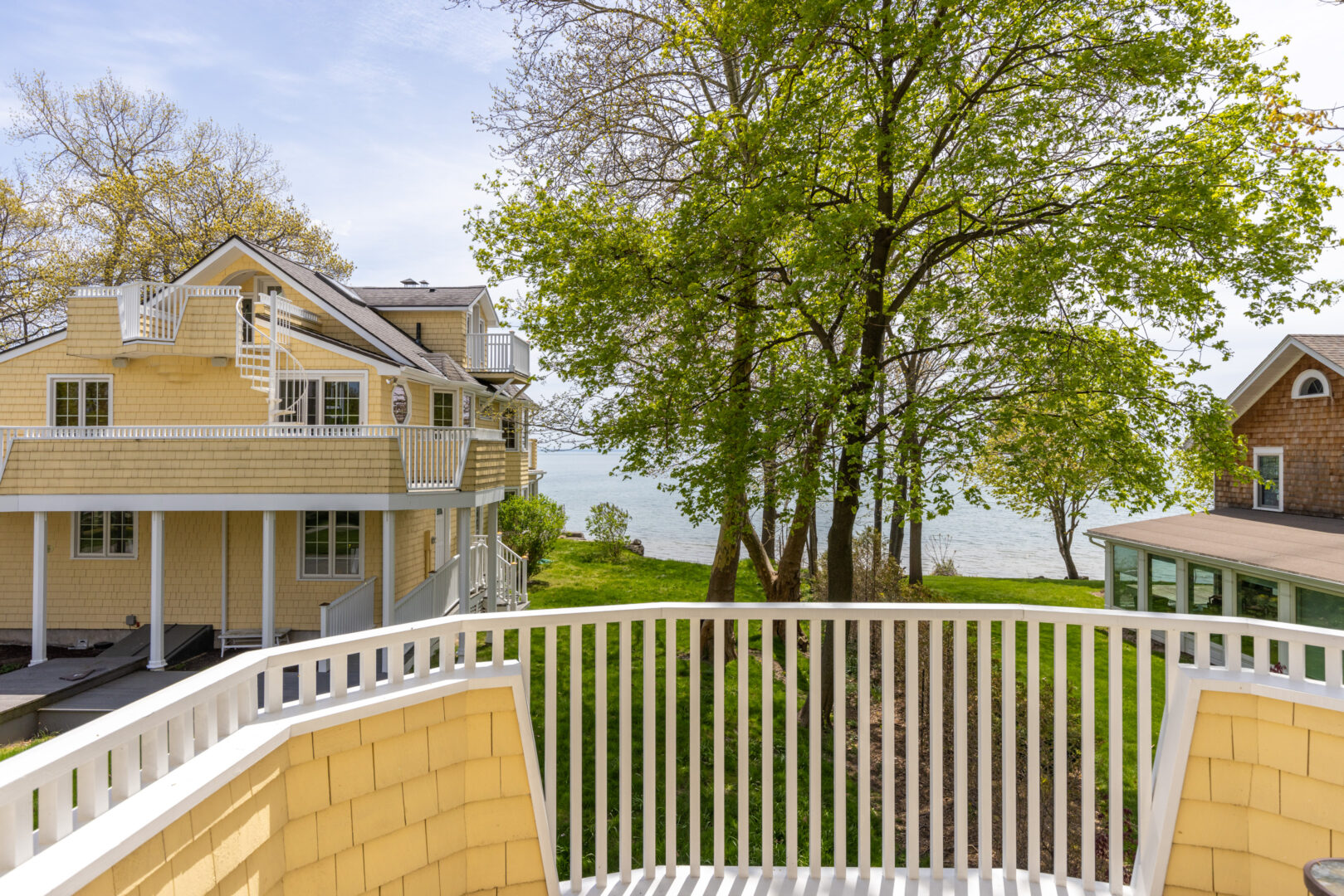 A round balcony with a white railing, looking out to a large lake house.