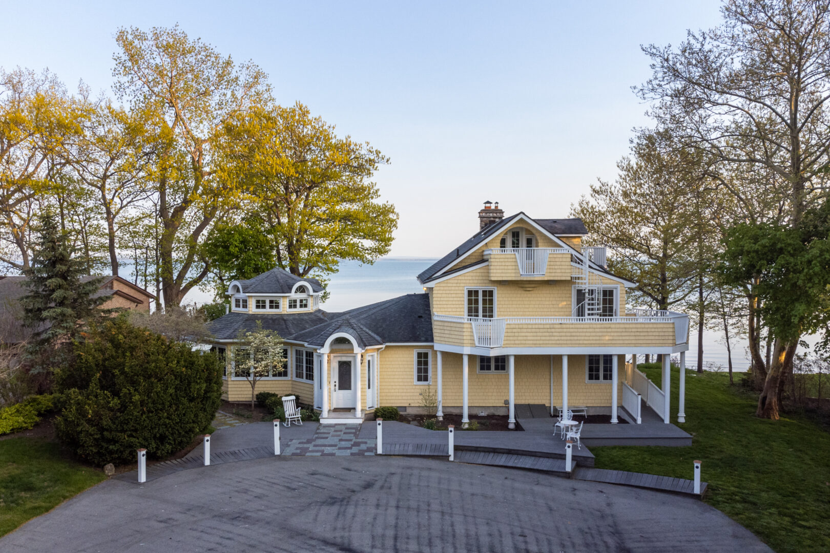 Front exterior of a large yellow cottage with white balconies and a paved driveway.