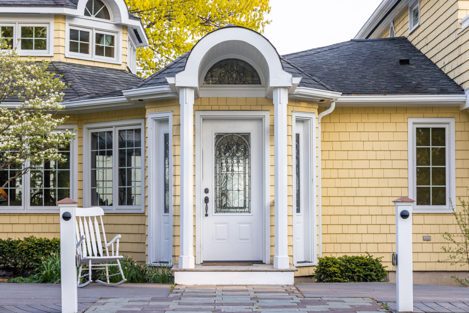 Front door of a large yellow cottage. A white archway leads to the white front door.