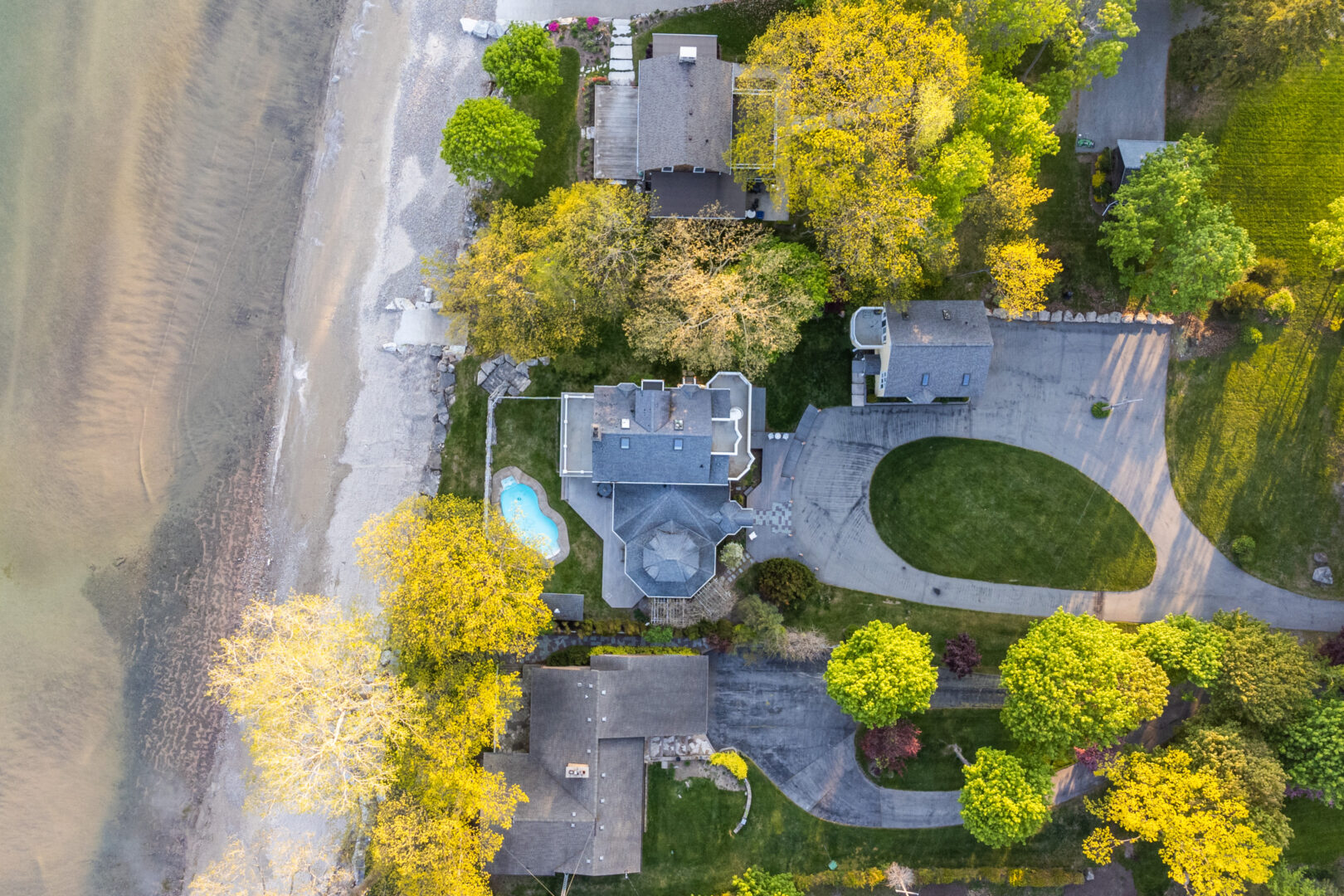 Aerial view of a large lakefront property with two houses and an in-ground pool, surrounded by trees.