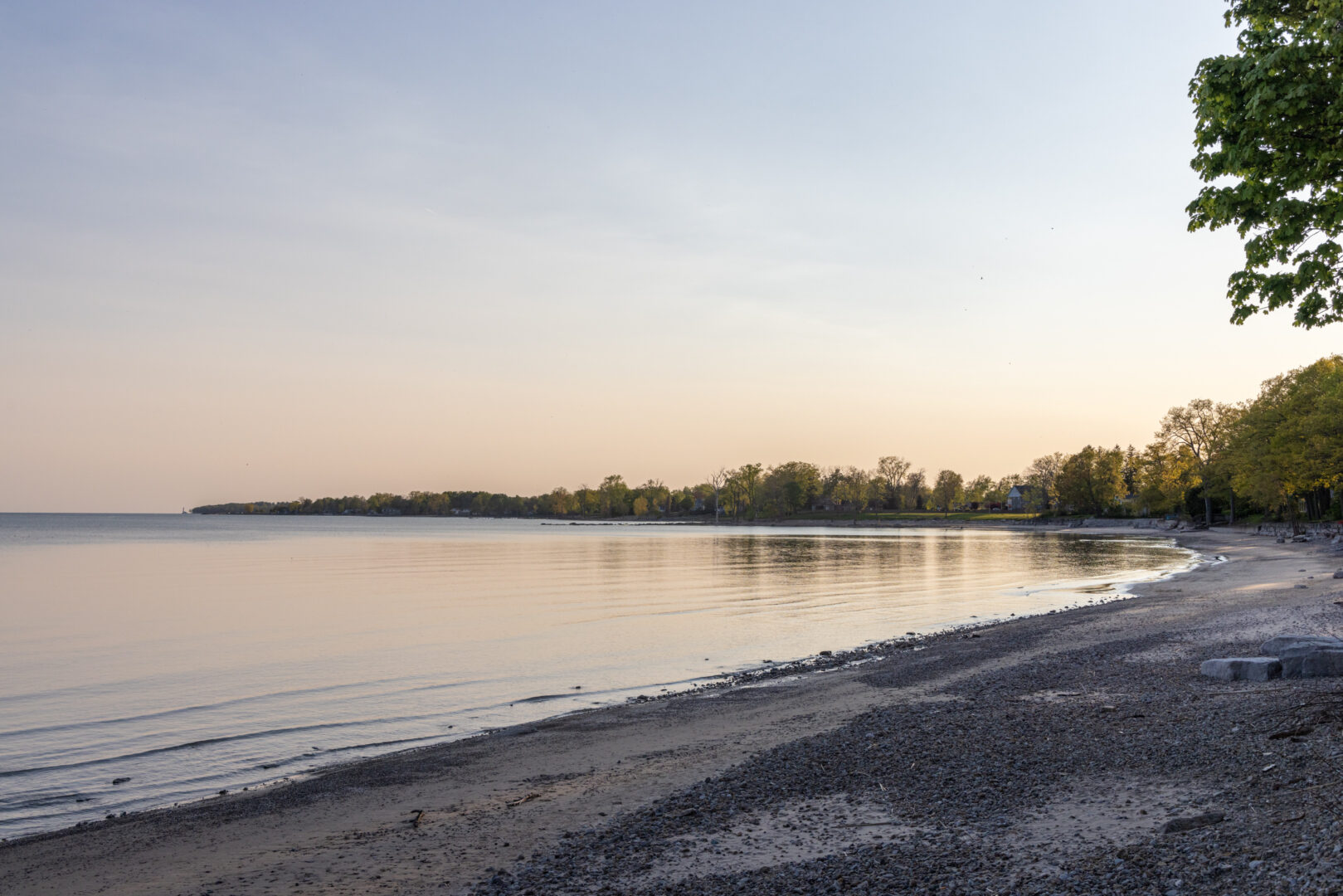 A sandy shoreline looking out over a calm lake at sunset.