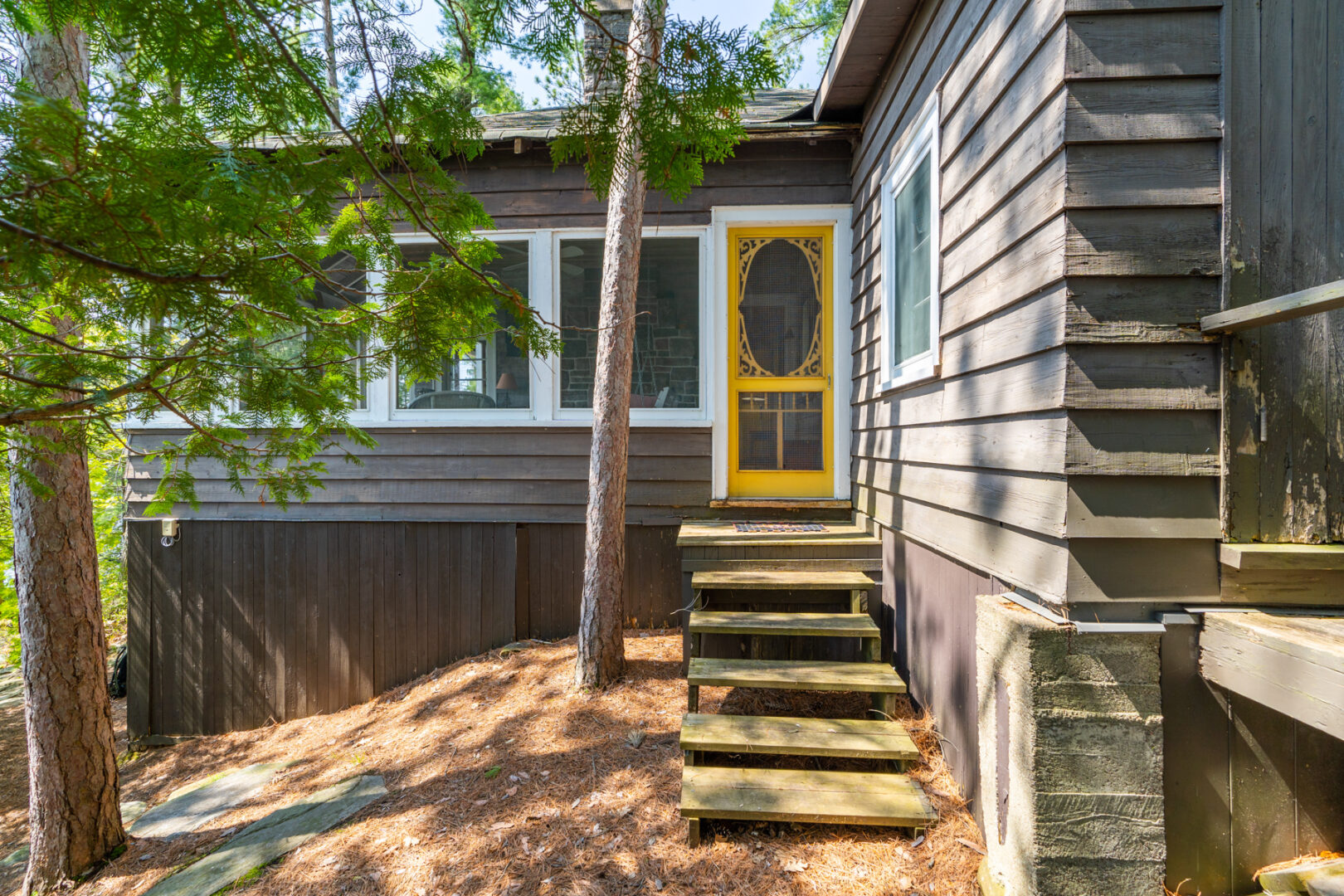 Stairs lead up to a yellow screen door that enters into a cottage sunroom.