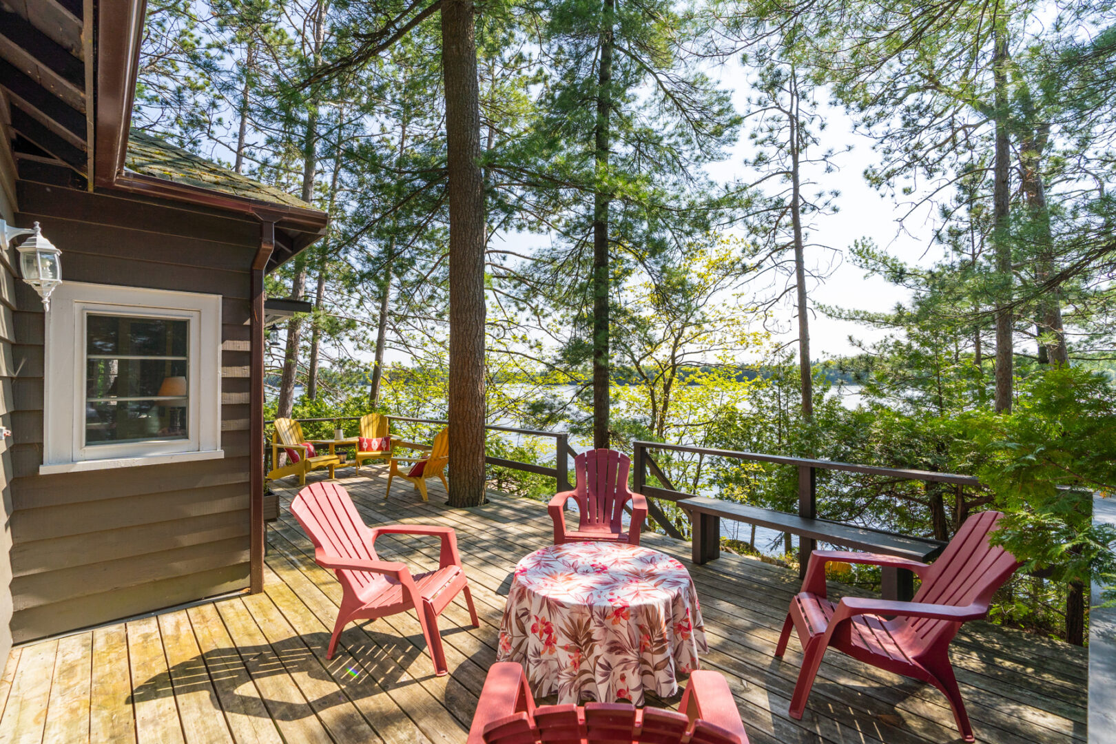 A large deck with two sets of Muskoka chairs, extending off the back of a cottage with a lake view.