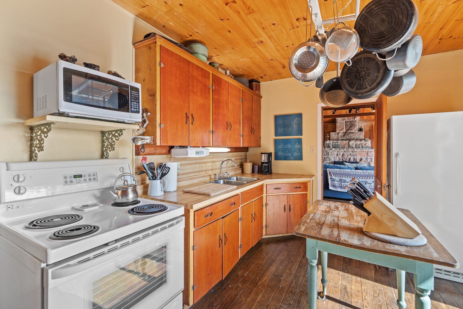 A small cottage kitchen with wooden cabinets, an oven, and pots and pans hanging from the ceiling.