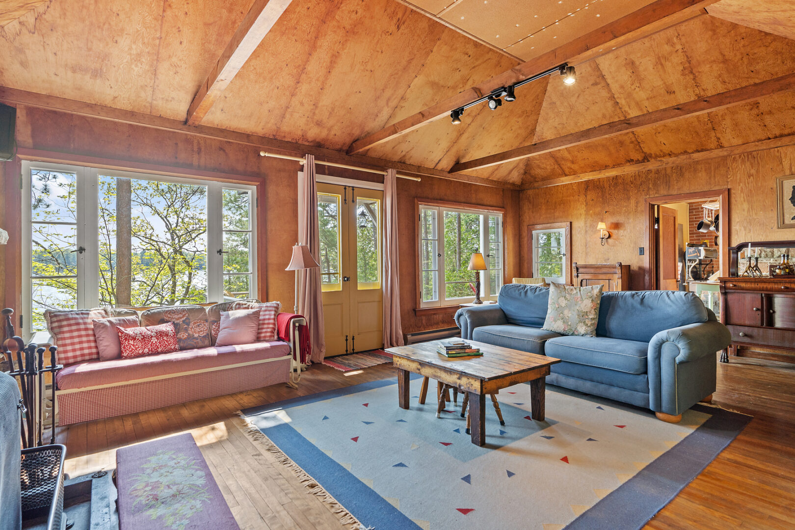 A bright, simple cottage living area with large windows, a blue couch, and double doors leading to a deck.