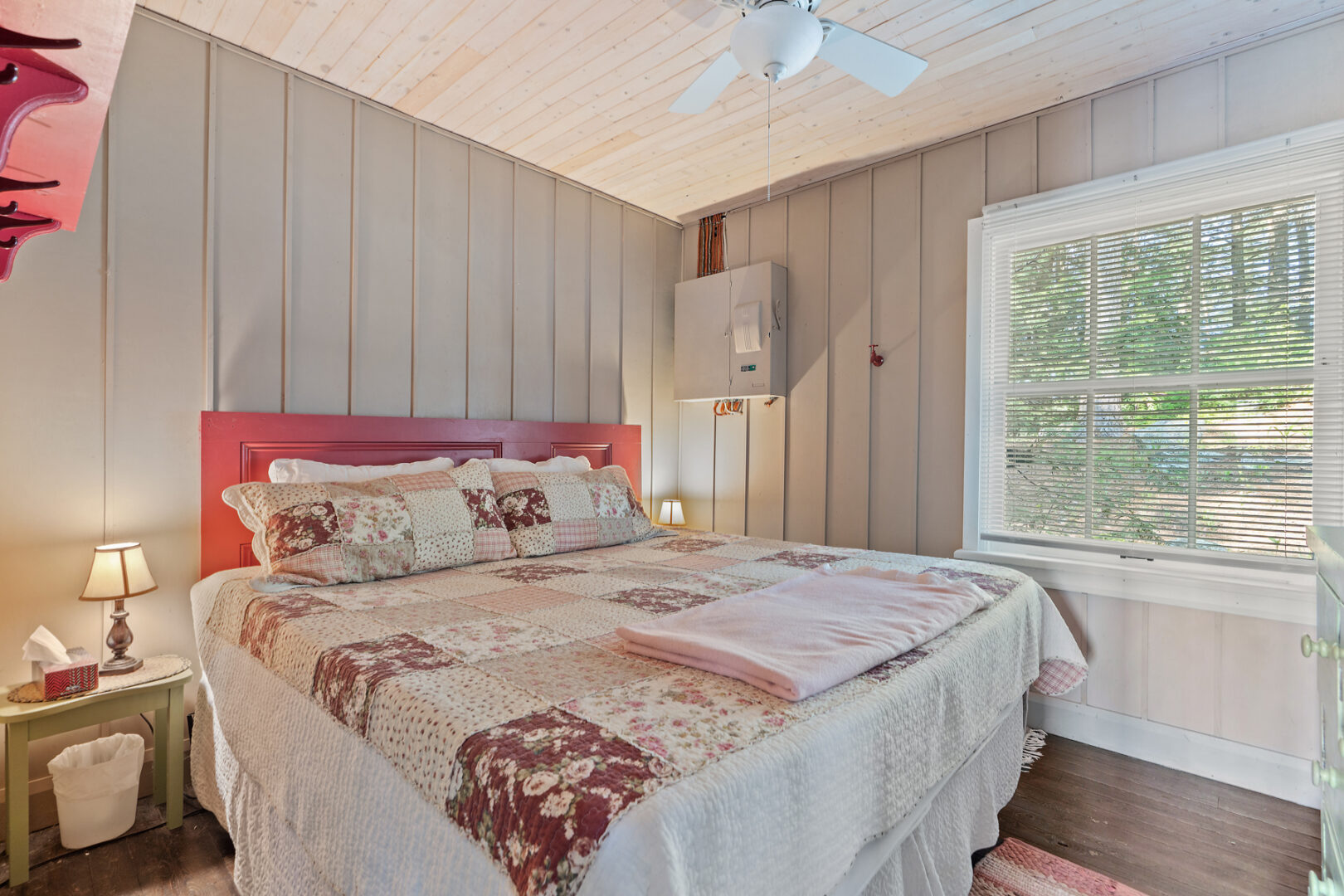 A bright bedroom with a big bed, which has a patchwork quilt bedspread, and a large window.