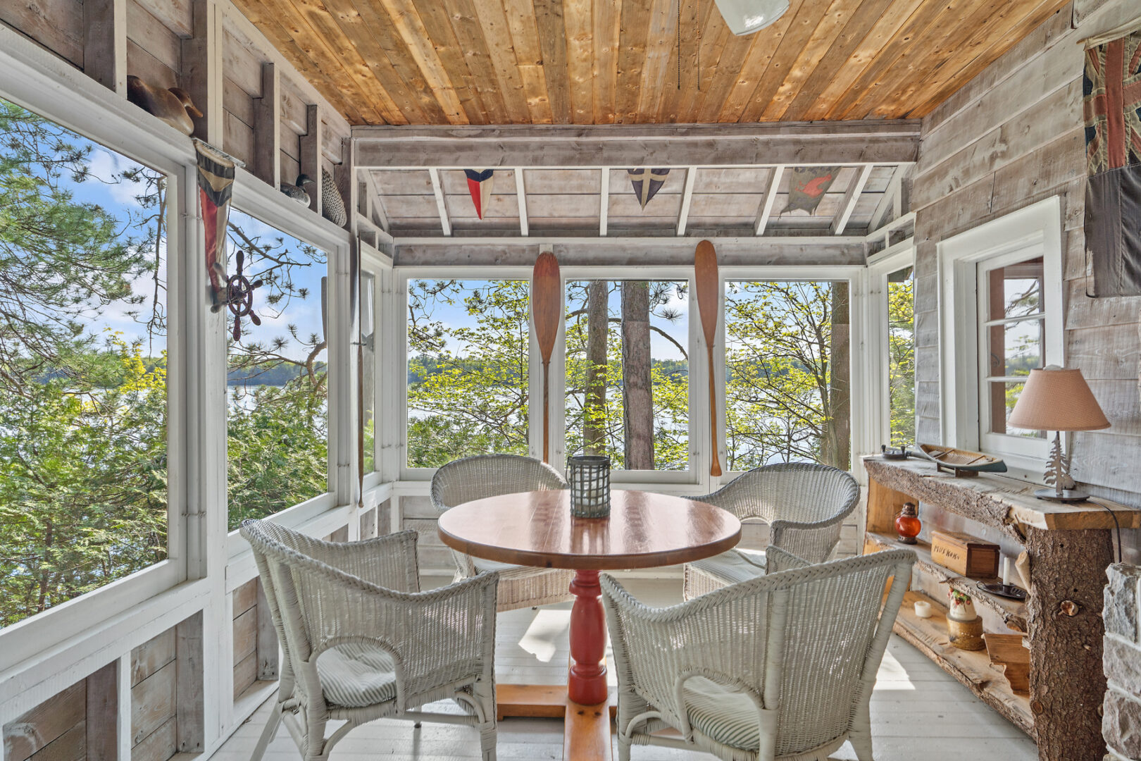 A bright cottage sunroom with white deck flooring and white wicker furniture.