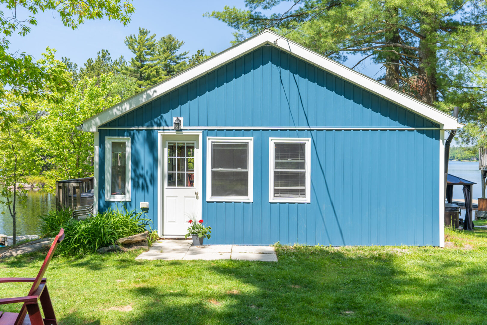 Front of a small blue cottage with a white front door and a green, grassy yard.