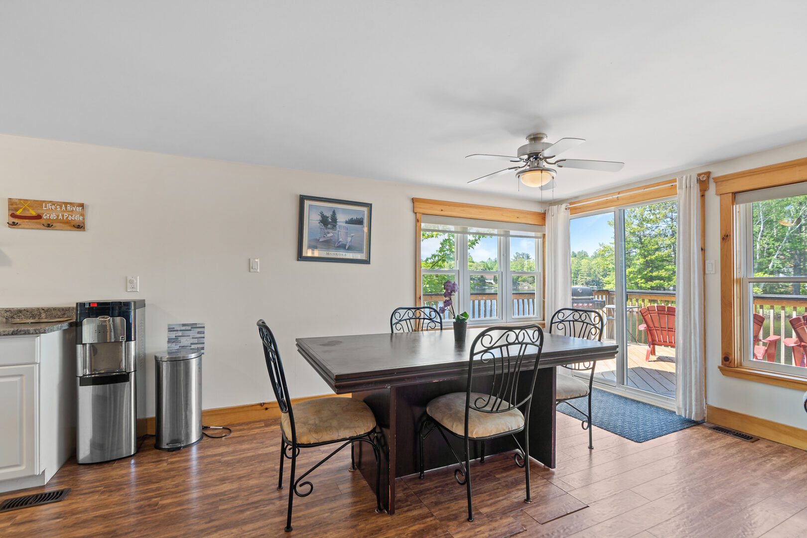 A dining table and chairs sits in front of big windows in a small cottage.