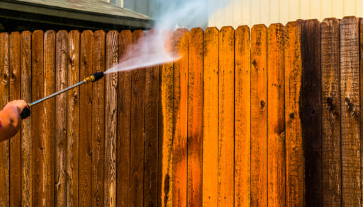 Someone pressure-washing a stained fence