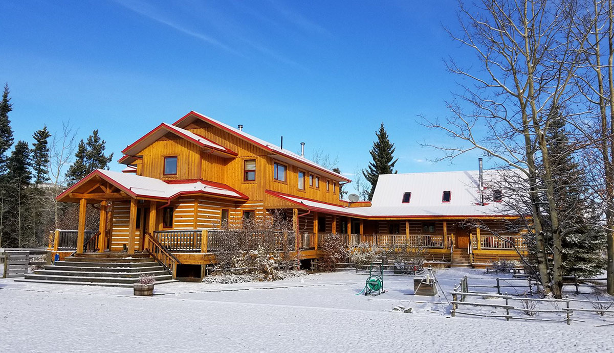 cabin exterior with orange wood and snow on the roof and lawn at midday