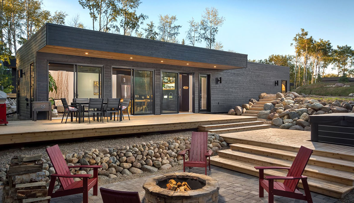 backyard with muskoka chairs around a fire in front of black sleek cottage