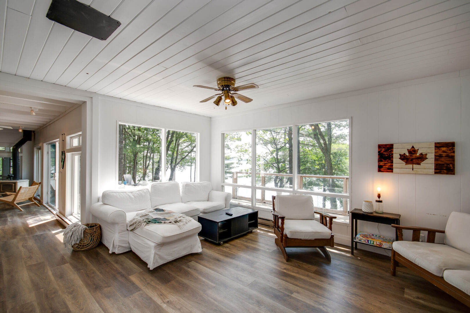 A bright cottage living area with hardwood floors, large windows, and white furniture.