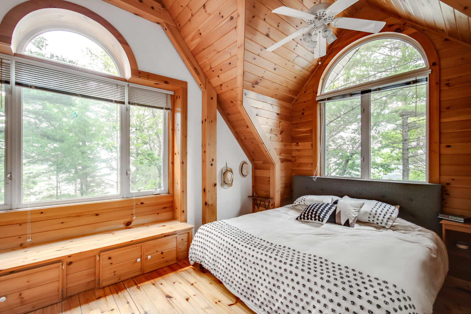 A large bedroom with wooden floors and a wood-panelled ceiling, a big white bed, and large windows.