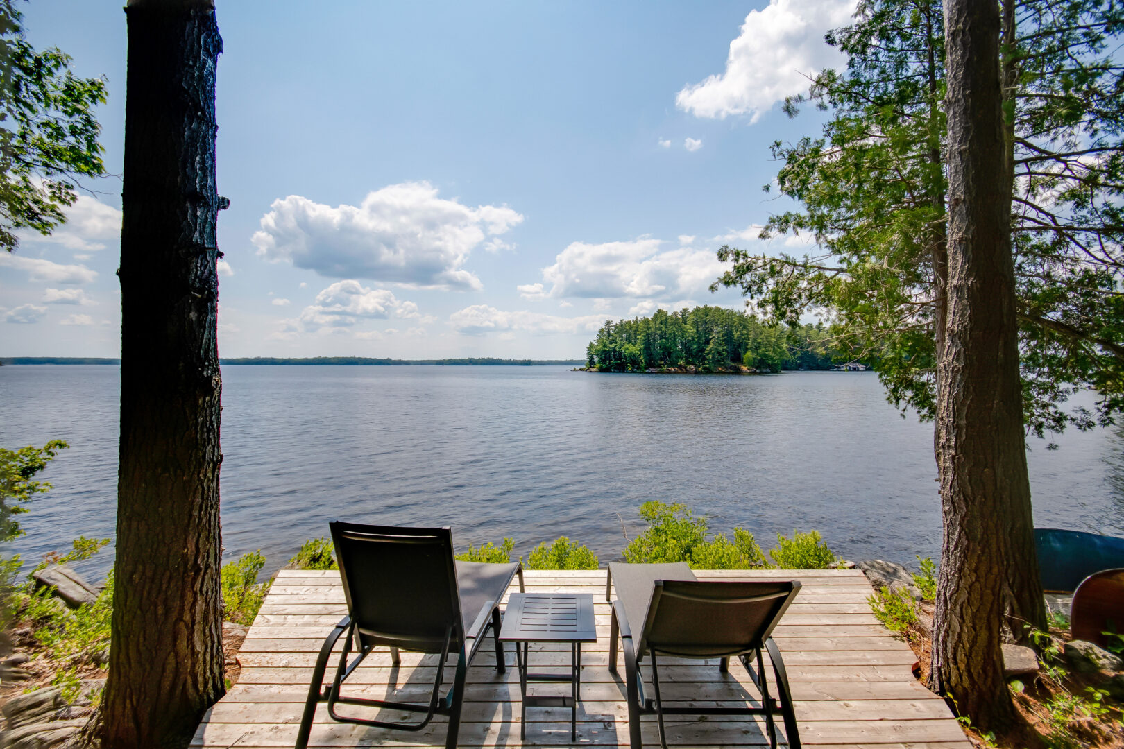 Two lounger chairs sit at the end of a small dock, looking out over the lake.