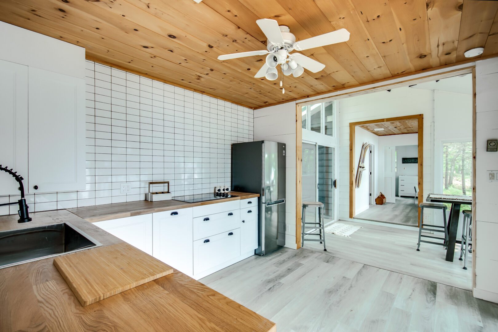 A small kitchen with wooden countertops, white cabinets, and a wood-panelled ceiling.