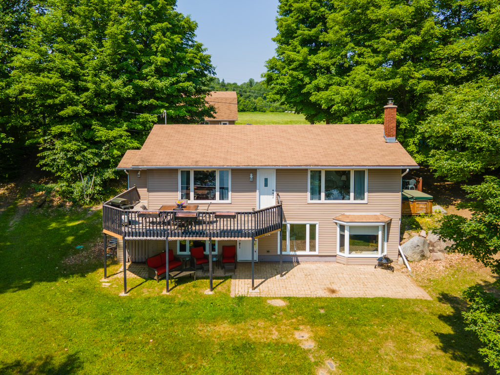 A two-storey house on a grassy property with lots of trees, with a patio on the ground and a deck extending off the second floor above it.