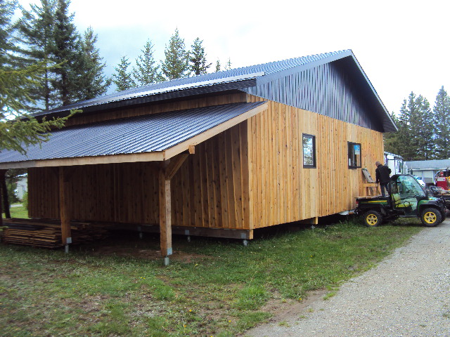 A large cedar garage on a grassy area. A large overhang extends off the side of the garage.