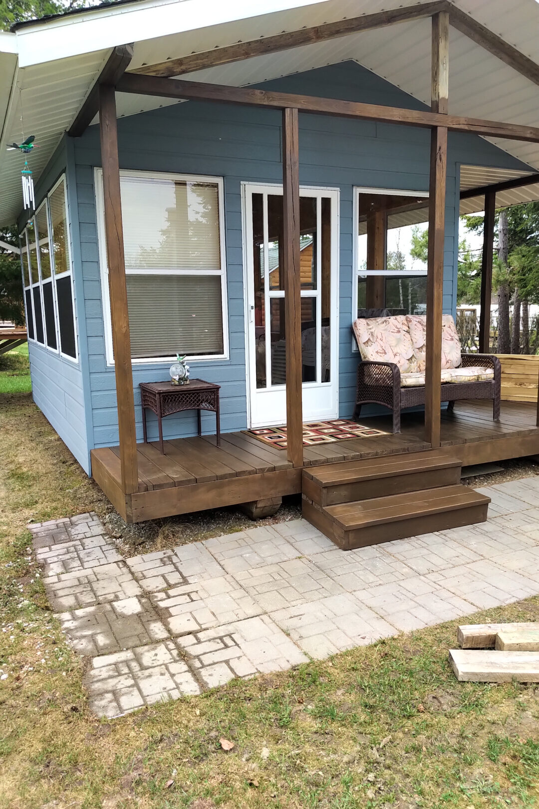 A tiny house with a blue exterior and a covered porch sits on a grassy lot.