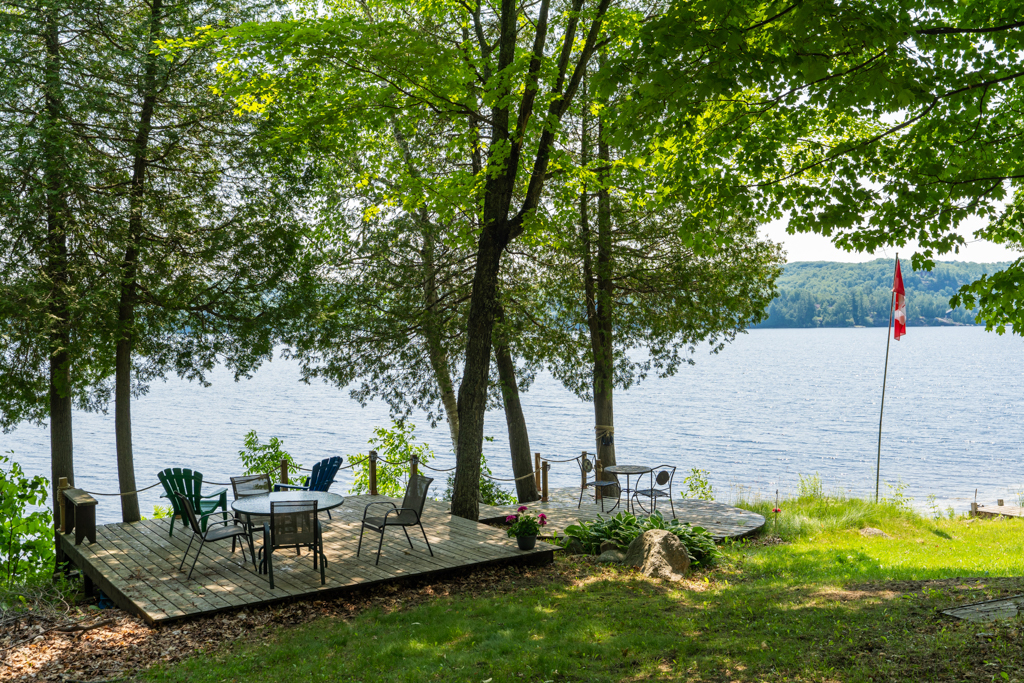 A small waterfront deck underneath shady trees, looking over a lake.
