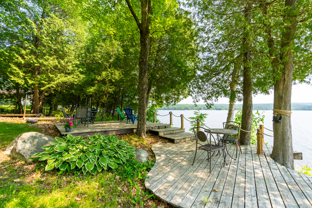A small waterfront deck underneath shady trees, looking over a lake.