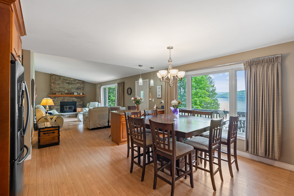 A bright dining and living area with a table and chairs, hardwood floors, and a big window.