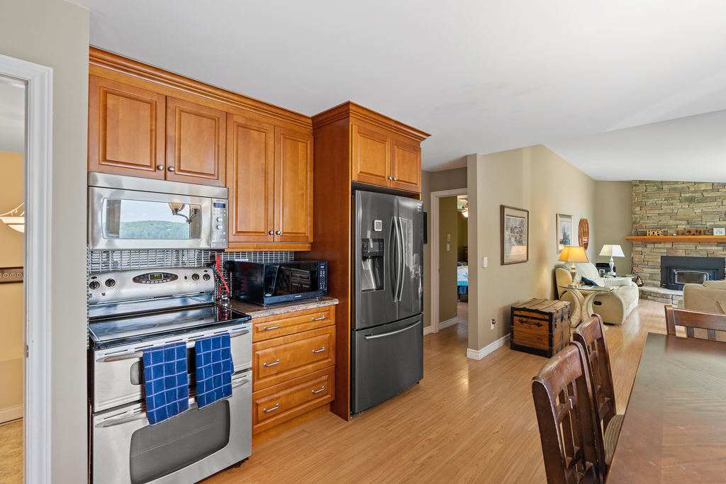A bright, open kitchen area with warm wood cupboards, a stainless steel oven an fridge, and hardwood floors.