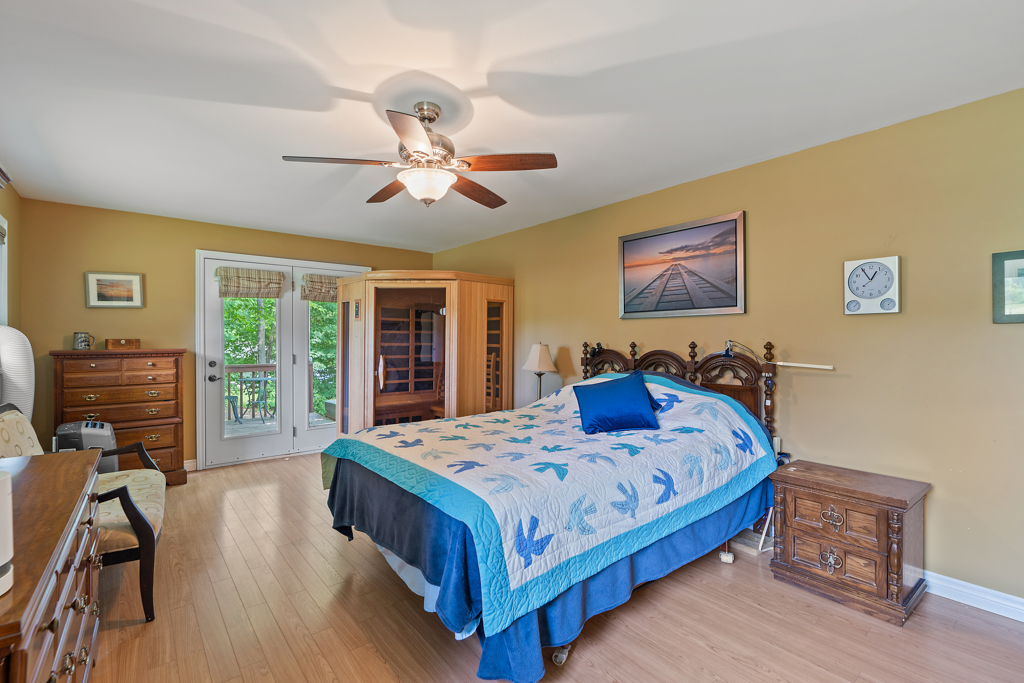 A big bedroom with a large bed, a ceiling fan, hardwood floors, and a double-door exit to a deck.