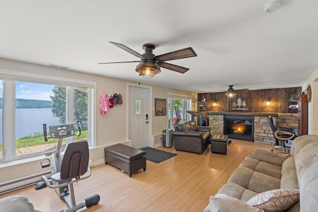 A long, bright living area with an exercise bench, a couch, a fireplace, and walkout doors to an outdoor patio.