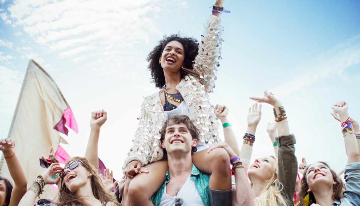 Woman cheering with one hand in the air, sitting on a man's shoulders at the front of a big crowd