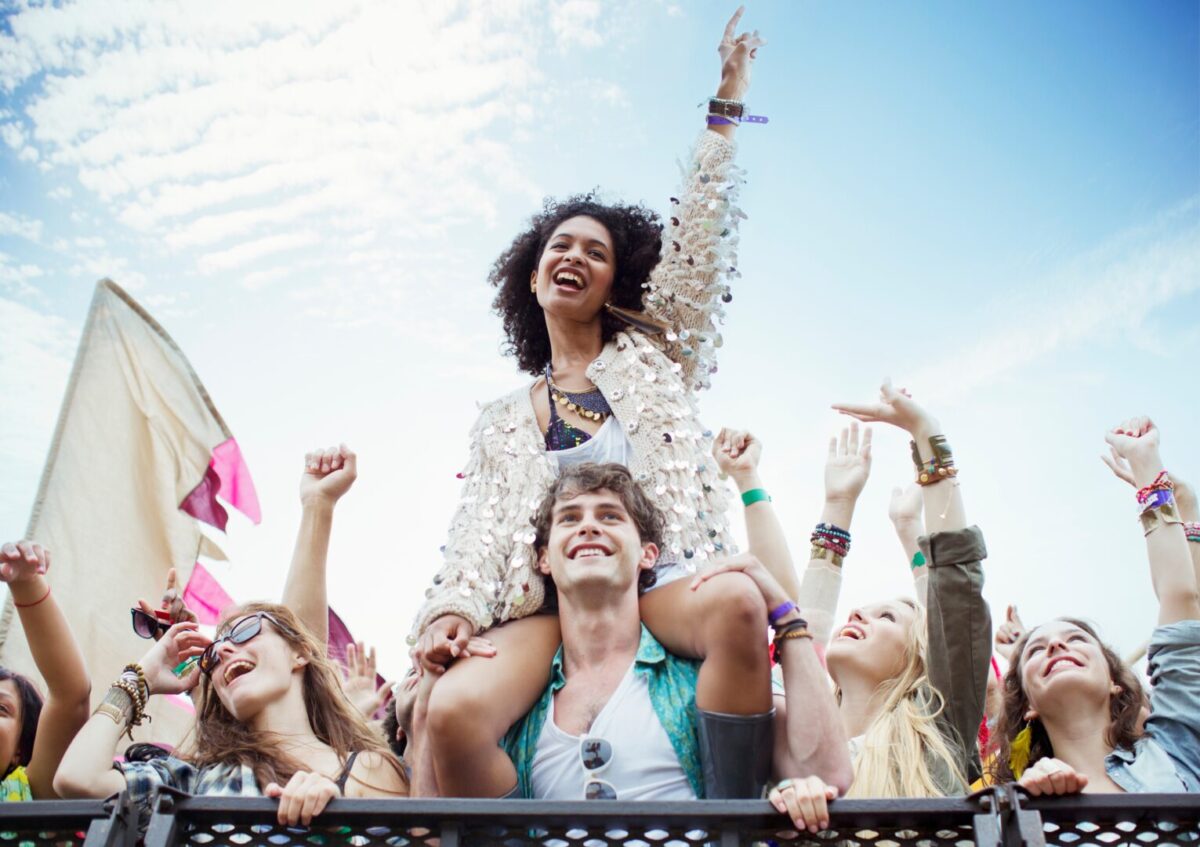Woman cheering with one hand in the air, sitting on a man's shoulders at the front of a big crowd