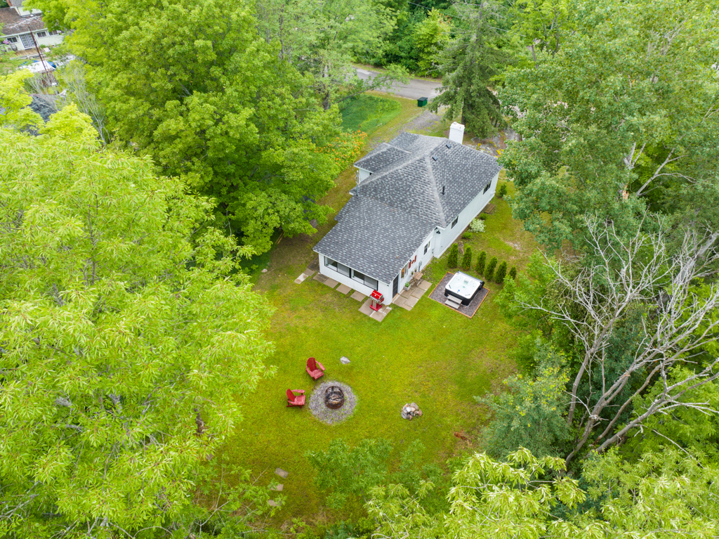 Overhead view of a small house with a gray roof and a big yard surrounded by trees.