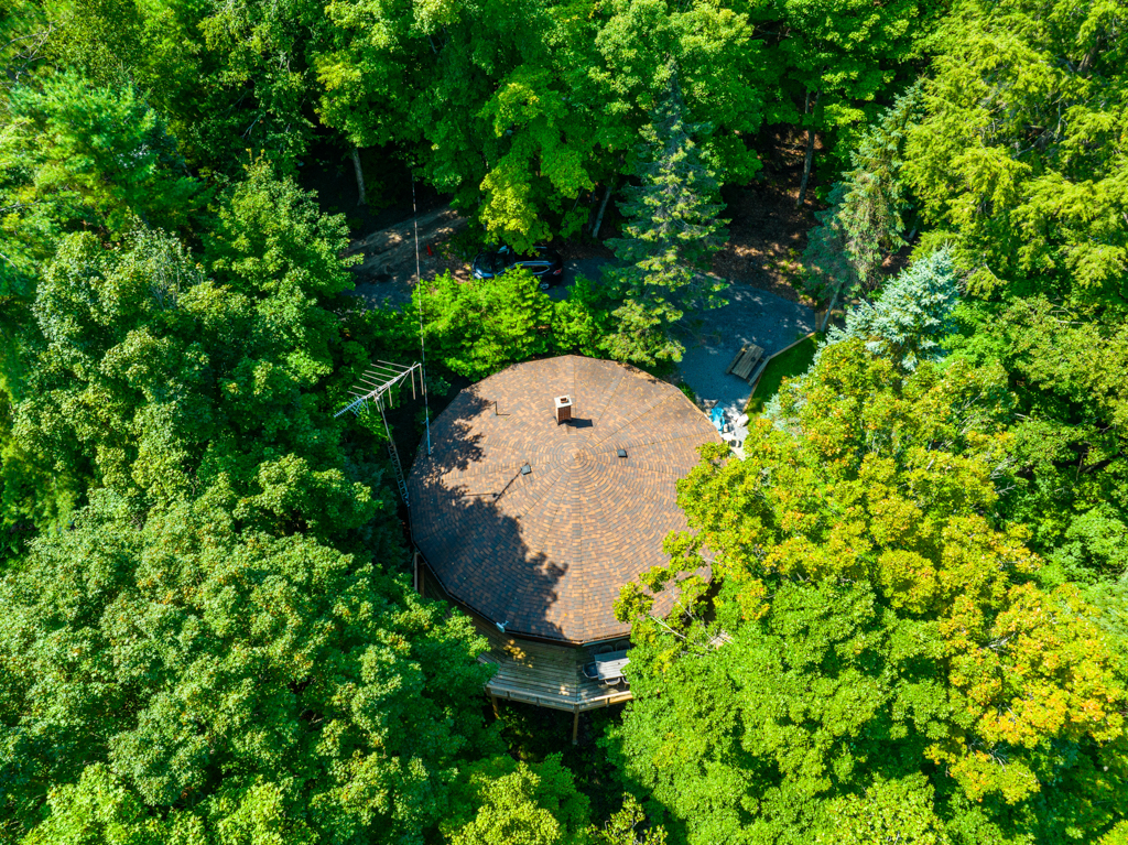 Overhead view of a circular cottage with a round roof, surrounded by green trees.