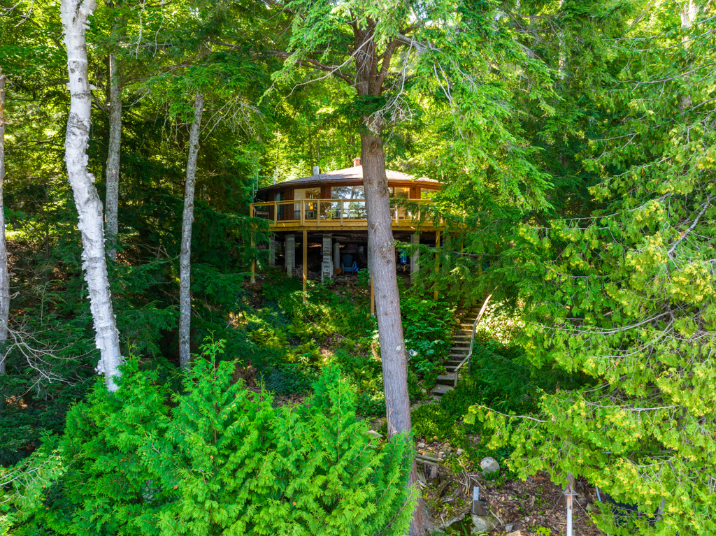 A round cottage with a big deck sits amongst green trees.