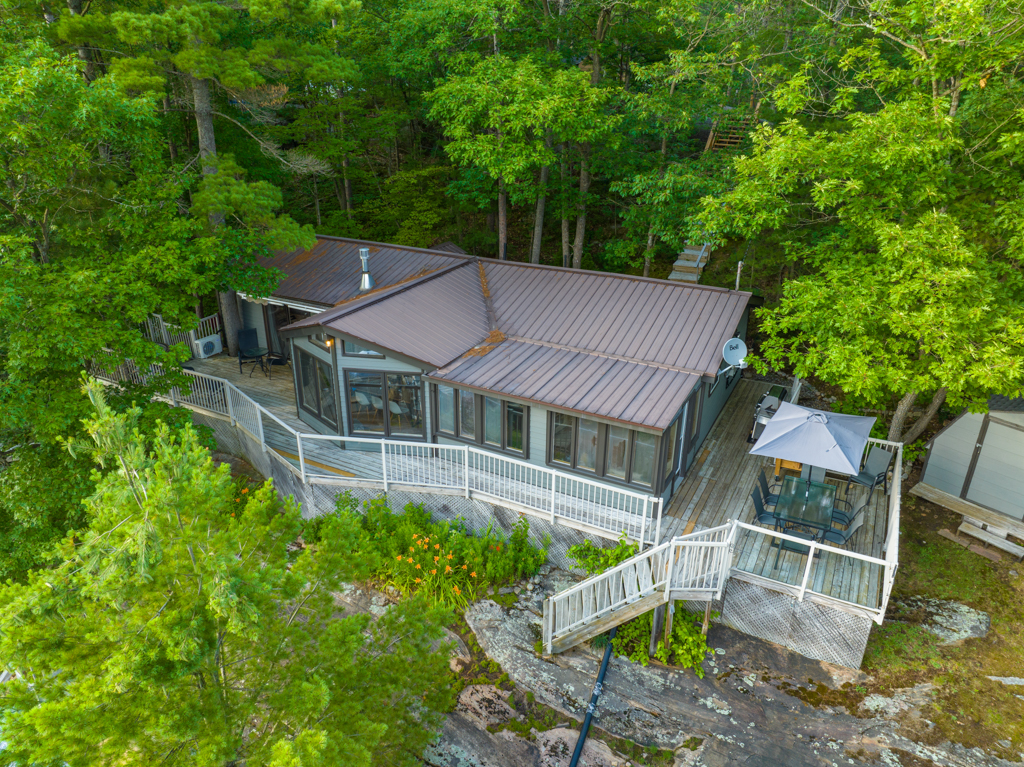 Overhead view of a big cottage with a long wrap-around deck, surrounded by trees.