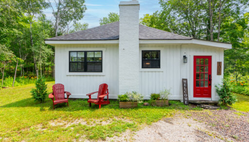 A small white house with a red door in a rural area.