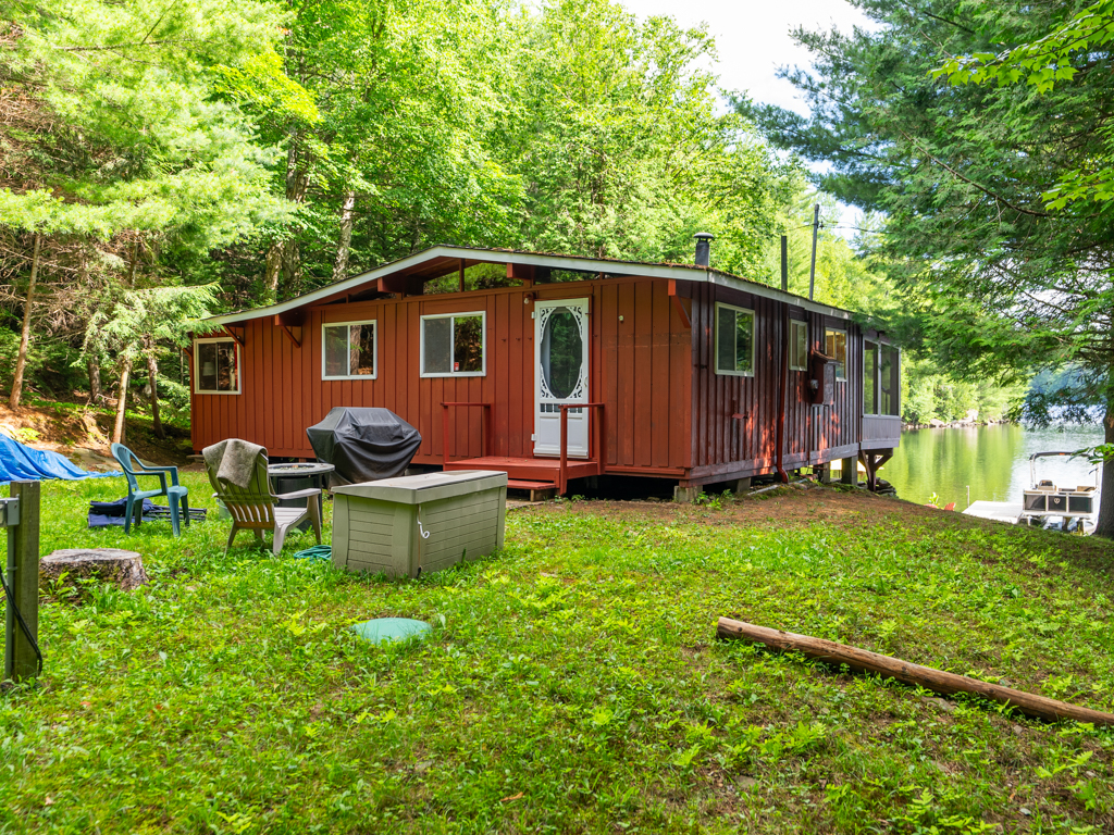 A small red cottage sits on a grassy lot, surrounded by trees.