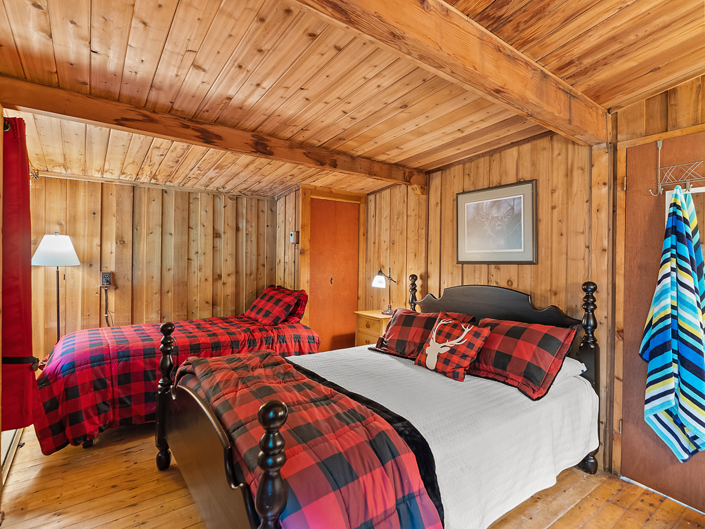 A bedroom with two beds that have red-and-black plaid bedding. The walls and ceiling are wood-panelled.