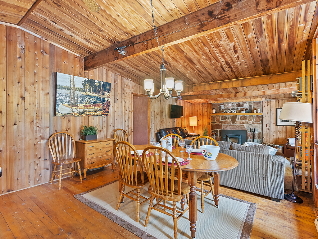 The interior space of a small cottage, with wood-panelled walls and ceiling, an open-concept plan, and a fireplace.