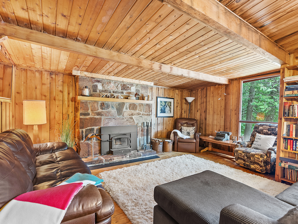 A granite fireplace in a wide, bright living area of a cottage with rustic decor.