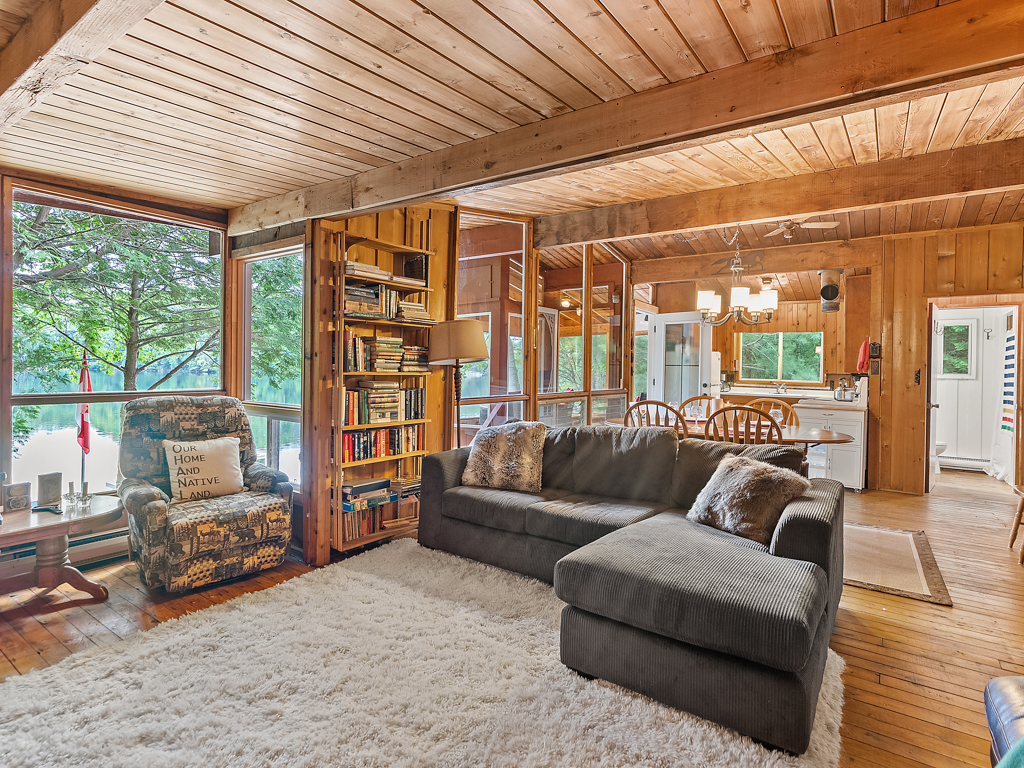 A couch and a chair sit next to a shelf of books in a bright, rustic cottage living space.