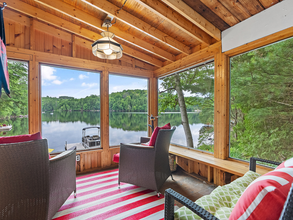 A sunroom with large windows overlooking a lake, with two chairs and a bench.