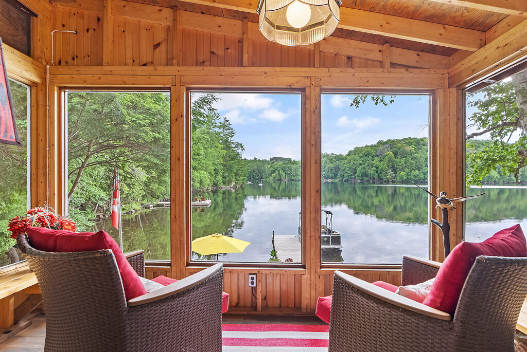 Two chairs facing the big windows of a sunroom, overlooking a lake view.