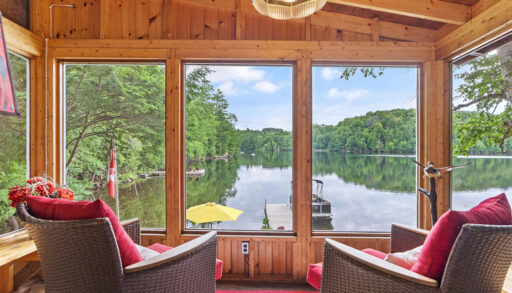 Two chairs facing the big windows of a sunroom, overlooking a lake view.