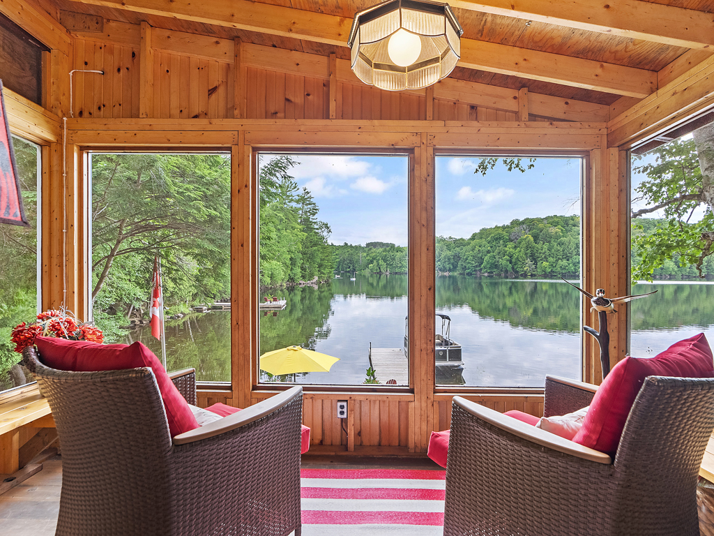 Two chairs facing the big windows of a sunroom, overlooking a lake view.