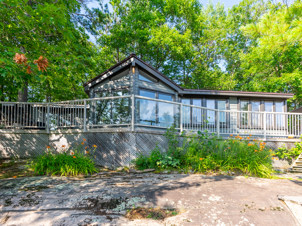 A big cottage sitting on a raised rock bed, with a deck and lots of windows.